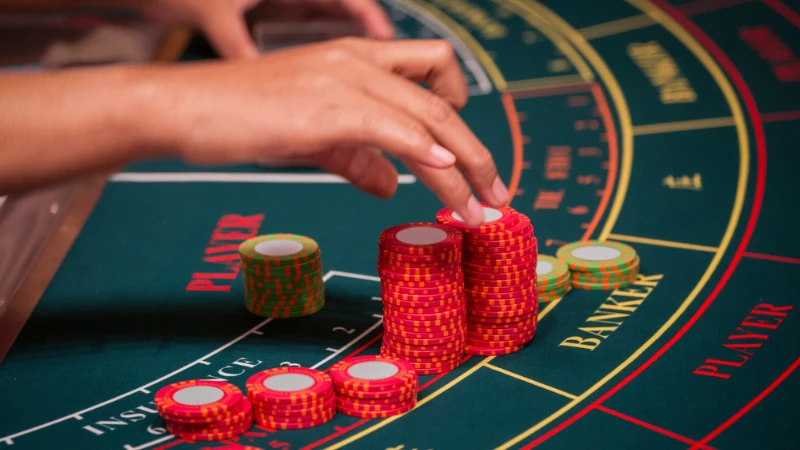 A Hand of Dealer Organizing the Red and Green Baccarat Chips on Baccarat Gaming table.